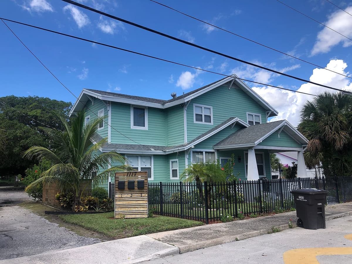 Two-story teal Florida home with palm trees on a residential street