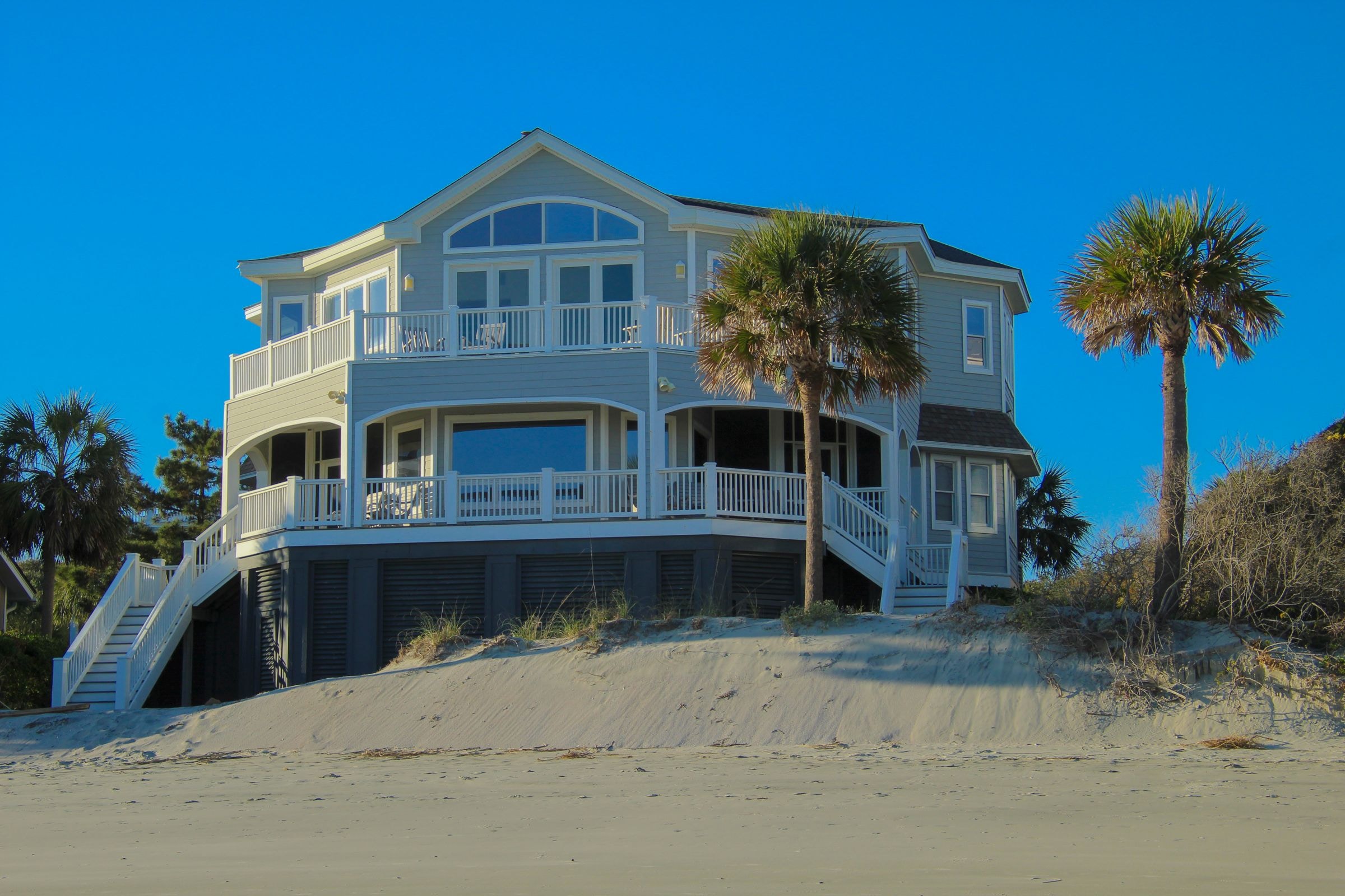 An expansive beachfront house with broad windows, wraparound balconies, palms and private stairs to the sand. Illustrative architecture, not a current listing.