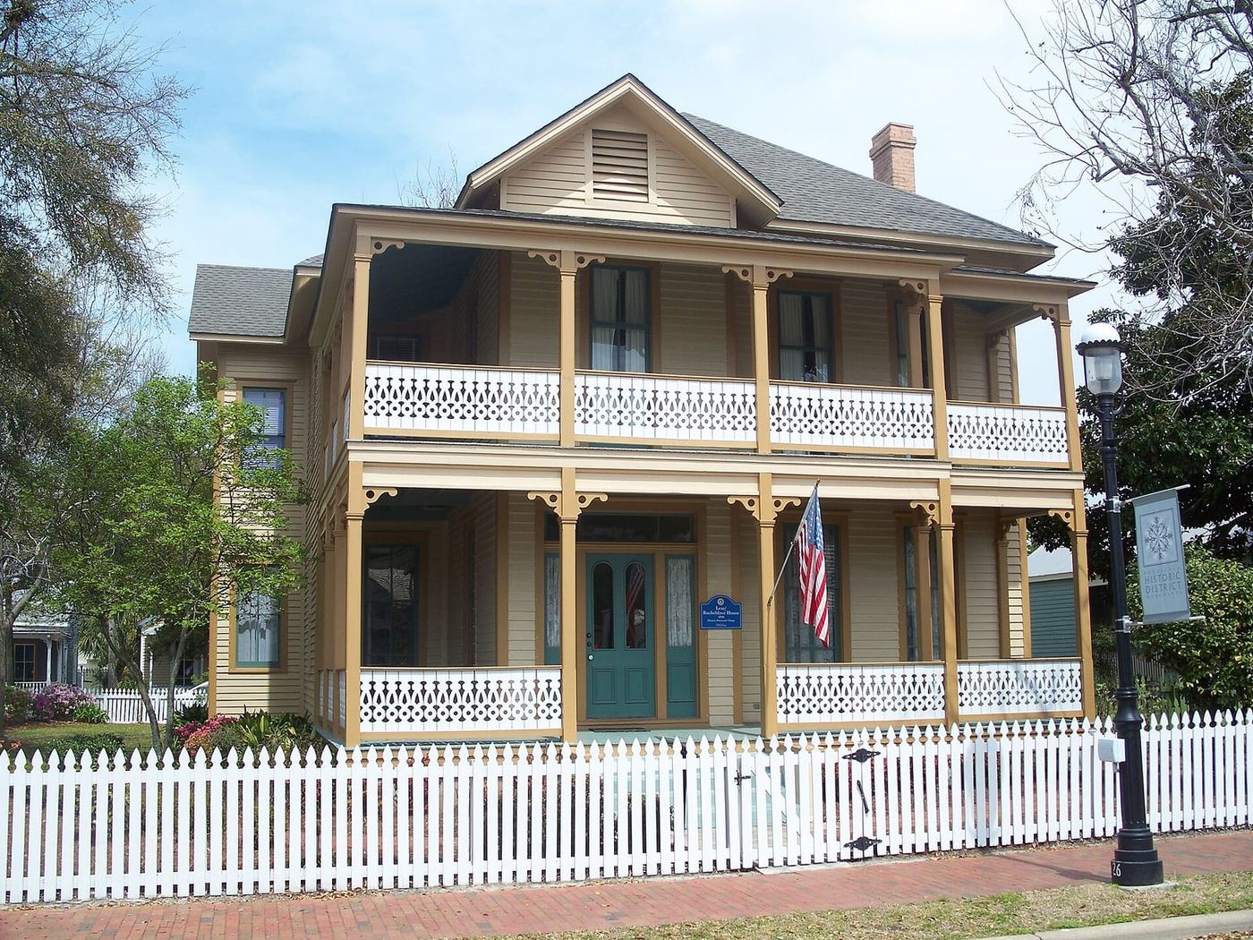 A restored two-story yellow Victorian house behind a white picket fence in the Pensacola Historic District